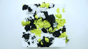 An image of a white canvas covered in black, yellow and white paper which has been thrown at the surface.