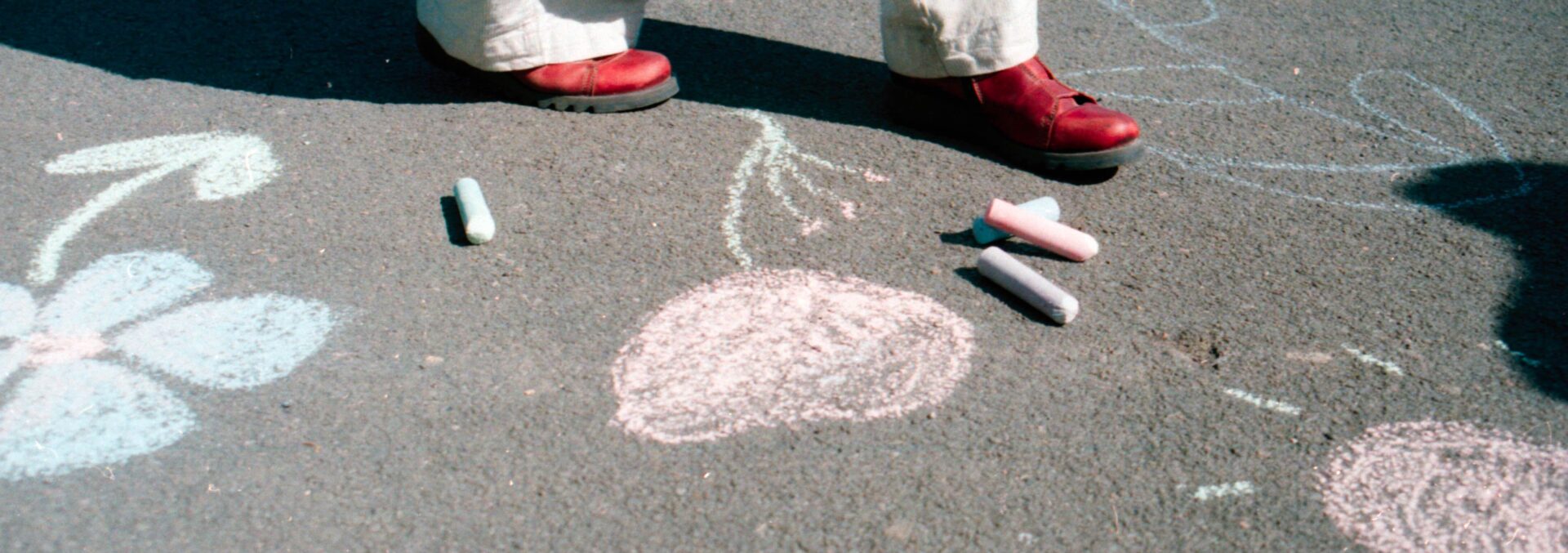 A school playground with different coloured chalk drawn into the tarmac. Someone is walking across, above their feet is cut out of the frame