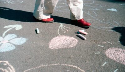 A school playground with different coloured chalk drawn into the tarmac. Someone is walking across, above their feet is cut out of the frame