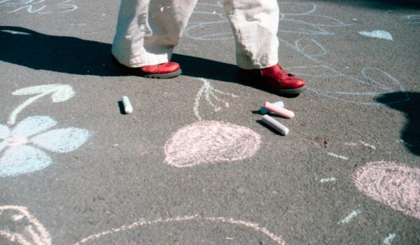 A school playground with different coloured chalk drawn into the tarmac. Someone is walking across, above their feet is cut out of the frame