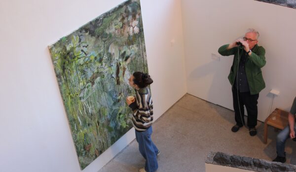 A large, green, abstract oil painting. A young woman wearign a green jumper and jeans is stood in front looking up at it.
