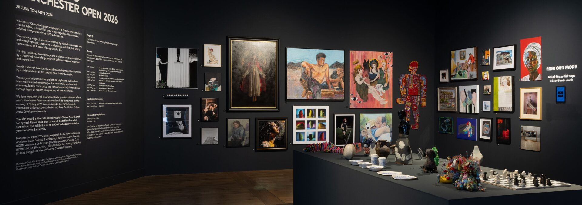 HOME Open. A dark gallery space with black walls, and lots of artwork hung from top to bottom.