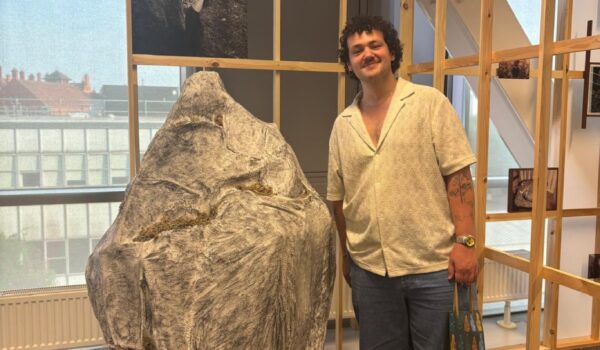 a man standing infront of a large wooden frame with a sculpture