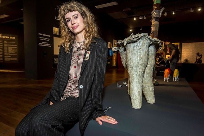 A young woman sat next to a sculpture at an exhibiton opening