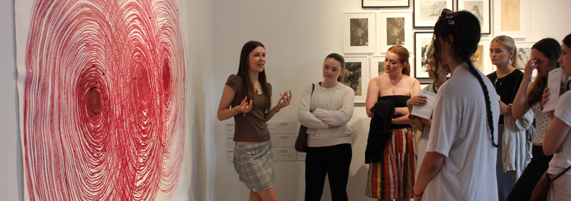 a student workshop, one is talknig to the group infront of a large oil pastel artwork of a spiral