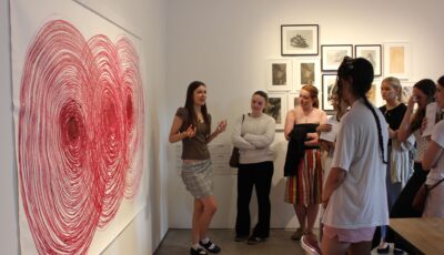 a student workshop, one is talknig to the group infront of a large oil pastel artwork of a spiral