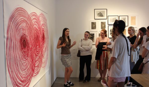 a student workshop, one is talknig to the group infront of a large oil pastel artwork of a spiral